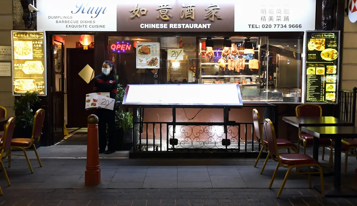 Pramusaji mengenakan masker berdiri di depan pintu sebuah restoran di Soho, di London, Selasa (22/9/2020). Perdana Menteri Inggris, Boris Johnson, telah mengumumkan bahwa pub dan restoran tutup pada pukul 10 malam, karena lonjakan kasus virus corona di seluruh Inggris. (AP Photo / Alberto Pezzali)