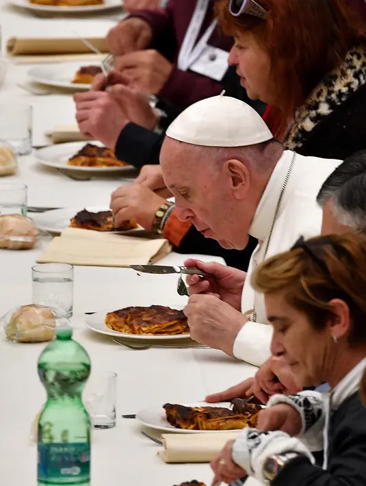 Paus Fransiskus (kanan) menyantap makan siang bersama sejumlah orang miskin di Pope Paul VI hall, Vatikan, Minggu (18/11). Makan siang bersama ratusan kaum papa, tunawisma, dan pengangguran itu memperingati Hari Orang Miskin Sedunia. (Vincenzo PINTO/AFP)