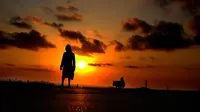 Seorang wanita dengan anjingnya berjalan di tepi laut saat matahari terbenam di resor pantai tenggara Ayia Napa di pulau Mediterania timur Siprus (11/3). (AP Photo/Petros Karadjias)