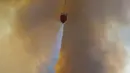 Sebuah helikopter menjatuhkan air saat berpartisipasi dalam operasi pemadaman kebakaran hutan di Koycegiz, Mugla, Turki, Senin (9/8/2021). Kebakaran hutan memaksa warga melarikan diri ke pantai untuk diselamatkan melalui laut. (AP Photo/Emre Tazegul)