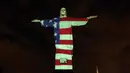 Patung Christ the Redeemer atau patung Yesus sang Penebus yang populer di dunia menyala dengan gambar bendera Amerika Serikat selama pandemi corona Covid-19 di Rio de Janeiro, Brasil, Minggu (12/4/2020). Tubuh patung itu dipenuhi gambar bendera, sekaligus pesan dan harapan. (CARL DE SOUZA/AFP)