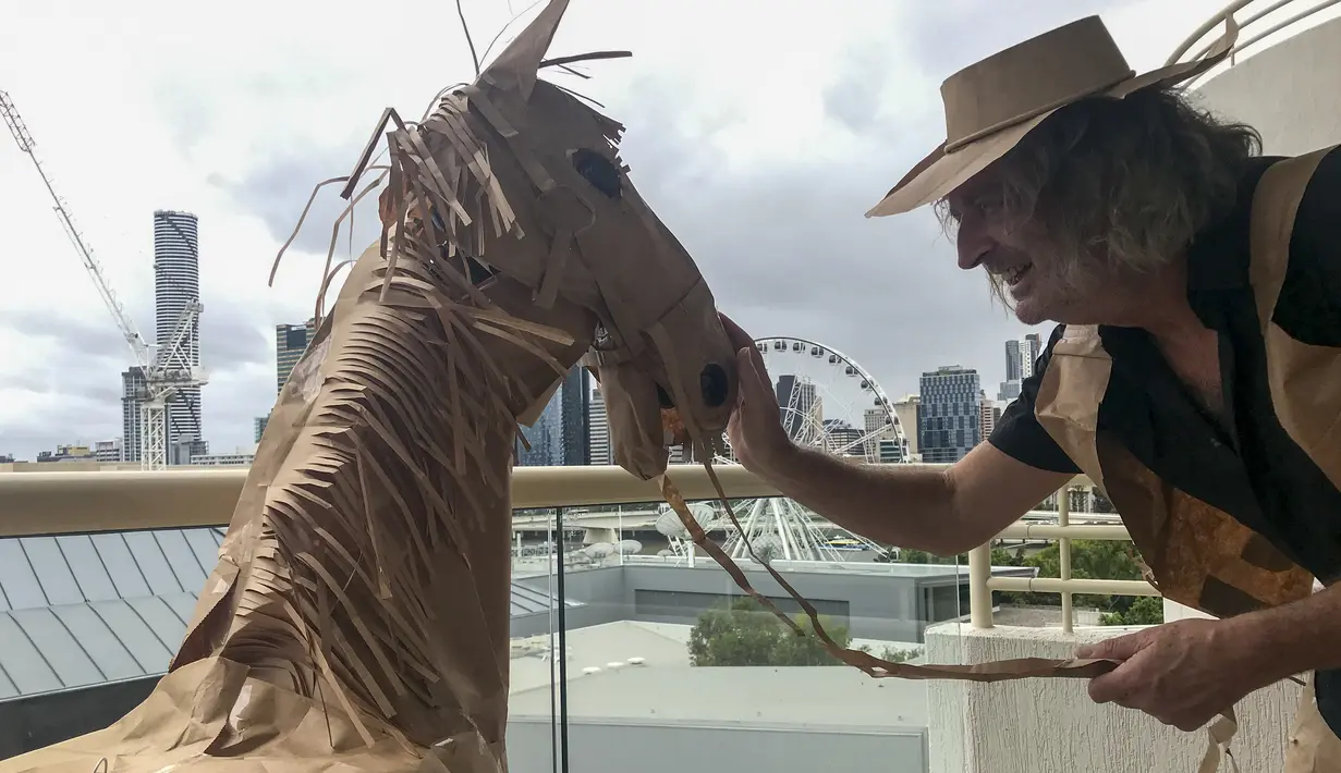 David Marriott berpose dengan kuda kertasnya Russell di kamar hotelnya di Brisbane, Australia, 3 April 2021. Direktur seni di iklan TV itu juga membuat pakaian koboi, celana topi dan juga rompi kantong kertas makanannya yang dikirimkan selama menjalani karantina. (David Marriott via AP)