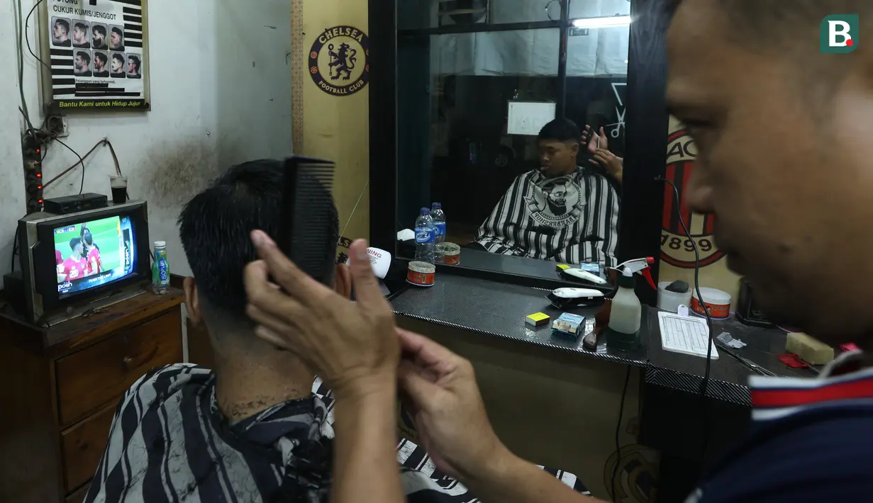 Tukang cukur rambut dan pelanggannya menyempatkan menonton pertandingan Timnas Indonesia vs Australia pada babak 16 besar Piala Asia di kawasan Pinang, Tangerang, Minggu (28/1/2024). Indonesia tumbang empat gol tanpa balas. (Bola.com/M Iqbal Ichsan)