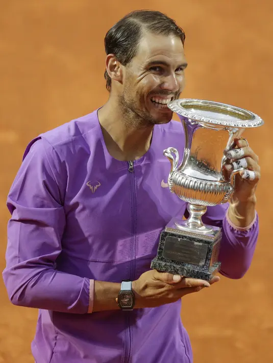 Petenis Spanyol, Rafael Nadal menggigit trofi juara turnamen tenis Italia Terbuka 2021 setelah mengalahkan petenis Serbia, Novak Djokovic di Foro Italico, Roma, Minggu (16/5/2021). Rafael Nadal menang dalam pertarungan tiga set 7-5, 1-6, dan 6-3 selama dua jam 49 menit. (AP Photo/Gregorio Borgia)
