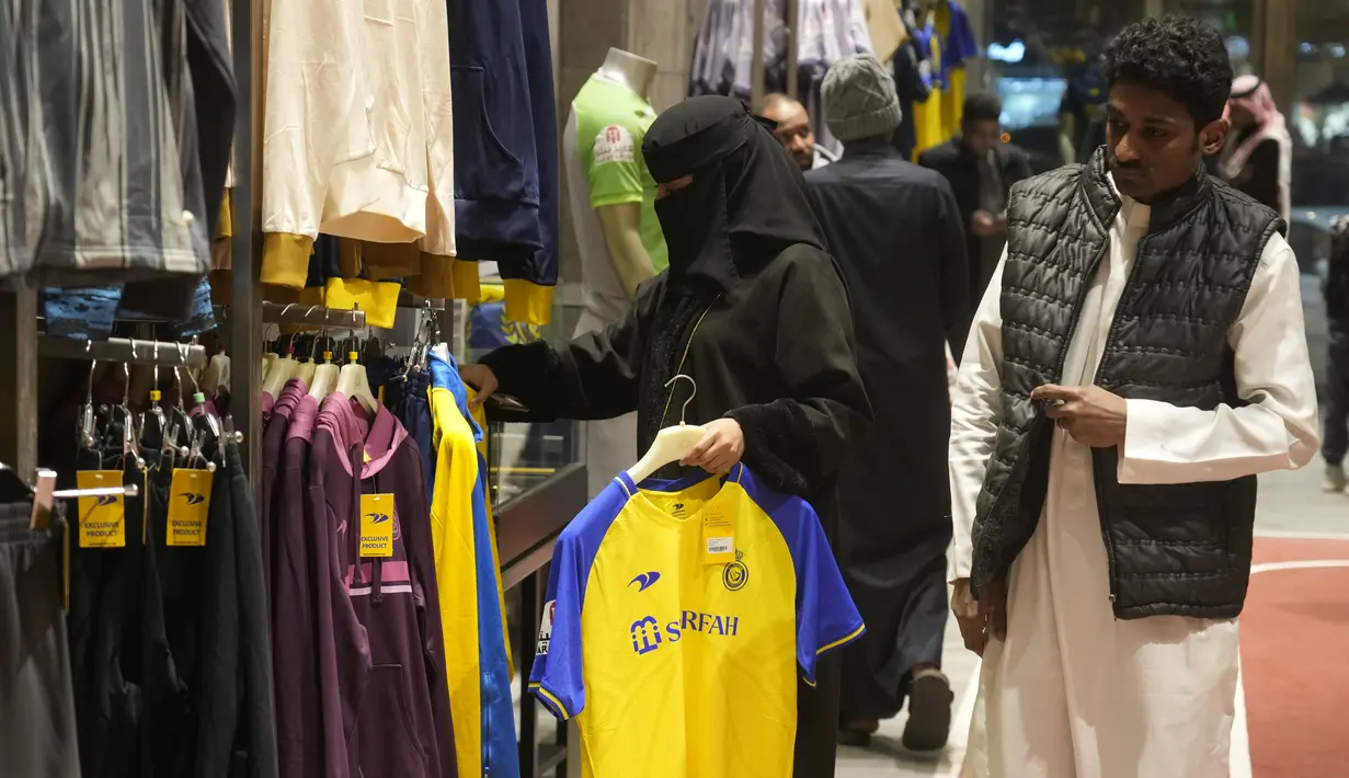 Seorang wanita memegang kaus Cristiano Ronaldo di toko klub Al Nassr di Riyadh, Arab Saudi, Senin, 2 Januari 2023. Antusiasme suporter berburu jersey sang megabintang dari Portugal itu membuat pemasukan tim bertambah. (AP Photo/Amr Nabil)