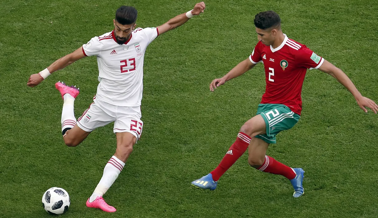 Aksi pemain Iran, Ramin Rezaeian (kiri) melepaskan tembakan saat diadang pemain Maroko, Achraf Hakimi (kanan) pada laga grup B Piala Dunia 2018 di St. Petersburg Stadium, Rusia, (15/6/2018). Iran menang 1-0. (AP/Darko Vojinovic)
