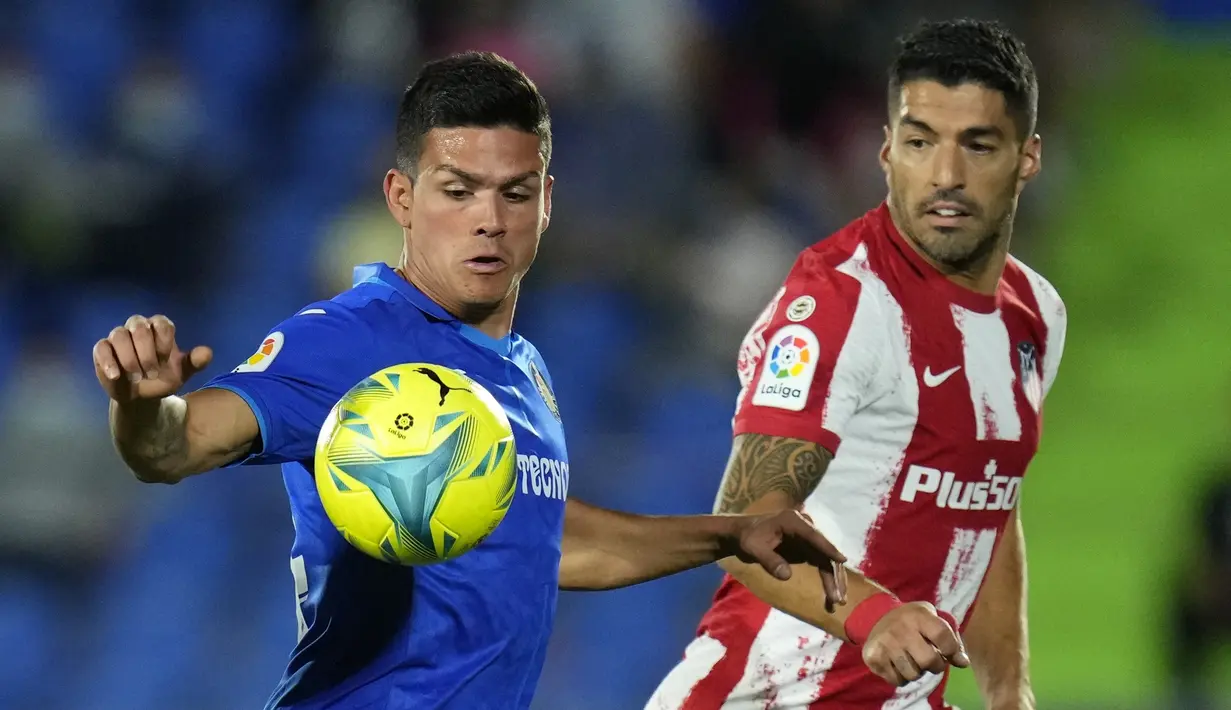 Bek Getafe, Jonathan Silva berebut bola dengan penyerang Atletico Madrid, Luis Suarez pada laga pekan keenam Liga Spanyol di Stadion Coliseum Alfonso Perez, Rabu (22/9/2021) dini hari WIB. Luis Suarez memborong dua gol saat Atletico Madrid mengalahkan Getafe 2-1. (AP Photo/Manu Fernandez)