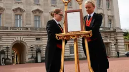 Senior footman Olivia Smith dan footman Heather McDonald saat memajang pengumuman kelahiran bayi baru kerajaan di halaman depan Istana Buckingham, London, Inggris, Senin (23/4). Kate Middleton melahirkan di RS St. Mary. (Pool Photo via AP)