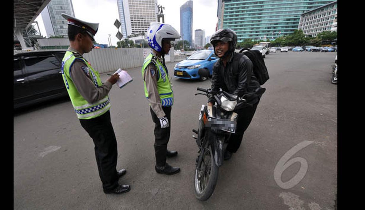 Petugas kepolisian menilang seorang pengendara motor yang menerobos Jalan MH Thamrin, Jakarta, Minggu (18/1/2015). (Liputan6.com/Miftahul Hayat)