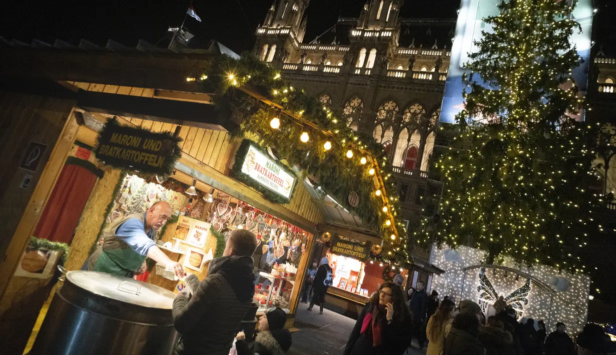 Seorang pria menjual chestnut asap dan kentang panggang di pasar Natal di depan balai kota Wina di Wina, Austria (19/11/2019). Setiap November hingga Natal tiba, Wina di Austria dikenal sebagai kota penyelenggara pasar malam Natal tertua di dunia. (AFP Photo/Joe Klamar)