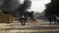 Seorang pria mengendarai sepeda motor melewati api menyusul protes di N'Djamena, Chad, Selasa (27/4/2021). Ribuan orang melakukan protes dan dua orang tewas dalam demonstrasi menentang aturan dewan militer transisi yang dipimpin putra Presiden Idriss Deby Itno yang terbunuh. (AP Photo/Sunday Alamba)