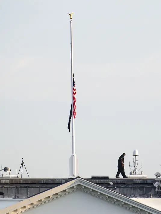 Petugas Secret Service berjalan kembali setelah menurunkan bendera AS yang berkibar setengah tiang di atas Gedung Putih, Kamis (26/8/2021). Pengibaran bendera AS setengah tiang itu untuk menghormati anggota marinir AS dan lainnya yang tewas dalam serangan bom di Kabul, Afghanistan (Eric BARADAT/AFP)