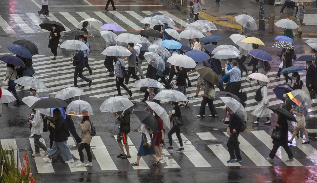 Para komuter yang mengenakan payung menyeberangi jalan saat  hujan yang dibawa oleh Topan Mindulle di Tokyo, Jepang, Jumat (1/10/2021). Topan Mindulle sedang bergerak di lepas pantai Jepang. (AP Photo/Kiichiro Sato)