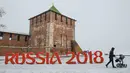 Seorang pria mendorong kereta dorong melewati lambang Piala Dunia 2018 yang ditempatkan di depan Kremlin, Nizhny Novgorod, Rusia, (21/1). Rusia akan menjadi tuan rumah Piala Dunia 2018. (Mladen ANTONOV/AFP)