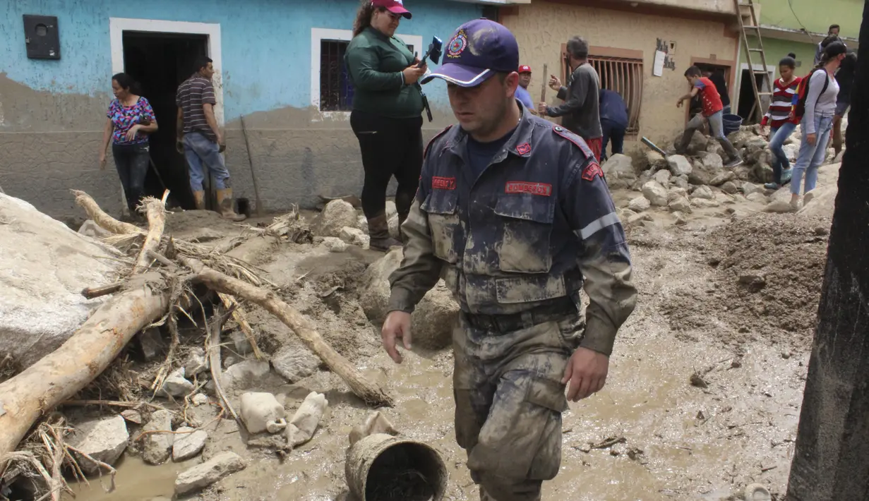 Petugas pemadam kebakaran berjalan di jalan yang rusak akibat banjir dan tanah longsor yang dipicu hujan lebat di Tovar, negara bagian Merida, Venezuela, Kamis (26/8/2021). Sedikitnya 20 orang tewas akibat hujan lebat banjir yang terjadi pada Rabu, 25 Agustus. (AP Photo/Luis Bustos)