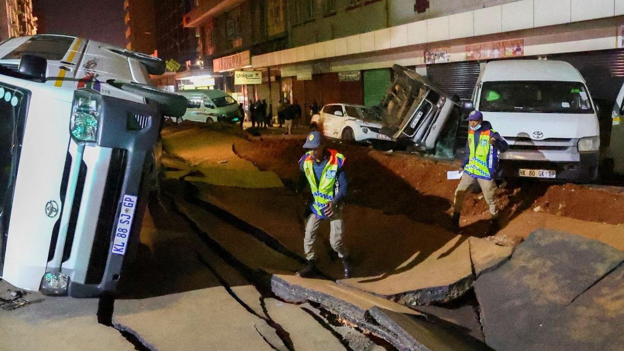 Sejumlah petugas polisi memeriksa keadaan mobil yang terbalik dan jalan yang rusak setelah ledakan gas bawah tanah terjadi di distrik pusat bisnis Johannesburg, Afrika Selatan (19/7/2023).
