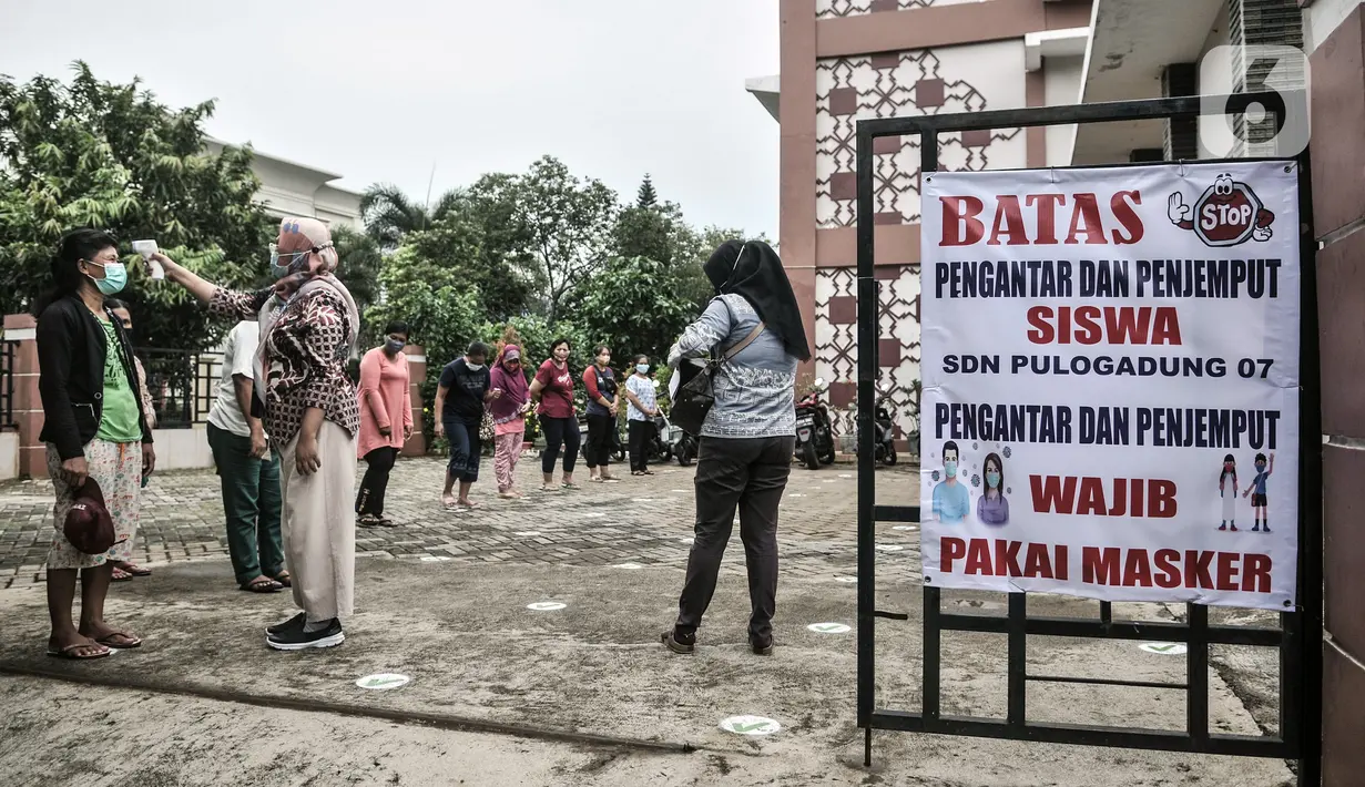 Tim Satgas COVID-19 bentukan pihak sekolah memeriksa suhu tubuh orangtua siswa saat hari pertama uji coba pembelajaran tatap muka di SDN Pulogadung 07, Jakarta, Rabu (7/4/2021). Pembelajaran tatap muka dilakukan di sekolah yang telah ditentukan. (merdeka.com/Iqbal S. Nugroho)