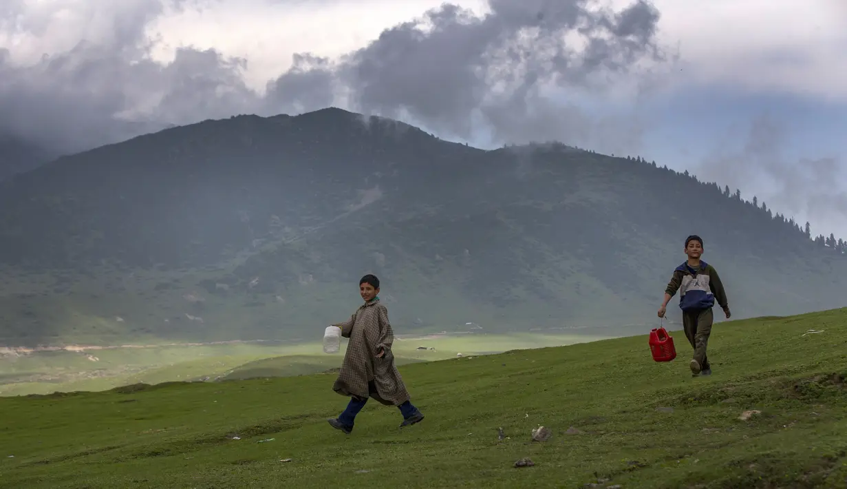 Anak-anak gembala Kashmir yang membawa kontainer plastik berjalan menuju mata air untuk mengambil air di Tosamaidan, barat daya Srinagar, Kashmir yang dikuasai India, Senin (21/6/2021).  Tidak hanya terkenal dengan padang rumputnya, Tosamaidan juga menjadi tujuan wisata. (AP Photo/Dar Yasin)