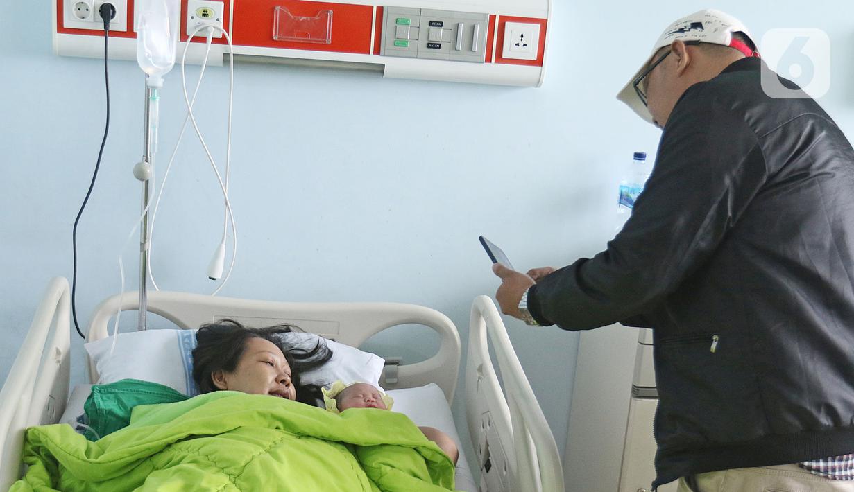 Andre (47) memotret istrinya Regina (43) usai melahirkan di RSUD Pasar Minggu, Jakarta, Kamis (20/2/2020). Bayi perempuan pasangan Regina dan Andre bernama Glowy Lidwina lahir di tanggal 20 bulan 02 tahun 2020 atau 20-02-2020. (Liputan6.com/Herman Zakharia)