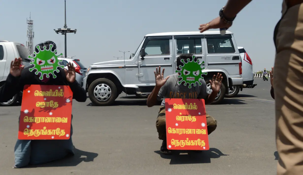 Dua pria mengenakan topeng bergambar virus corona dan memegang plakat bertuliskan "Jangan keluar, jangan mendekati corona" sebagai hukuman karena keluar rumah selama pemberlakukan penguncian wilayah (lockdown) di Chennai, India, Rabu (1/4/2020). (Arun SANKAR / AFP)