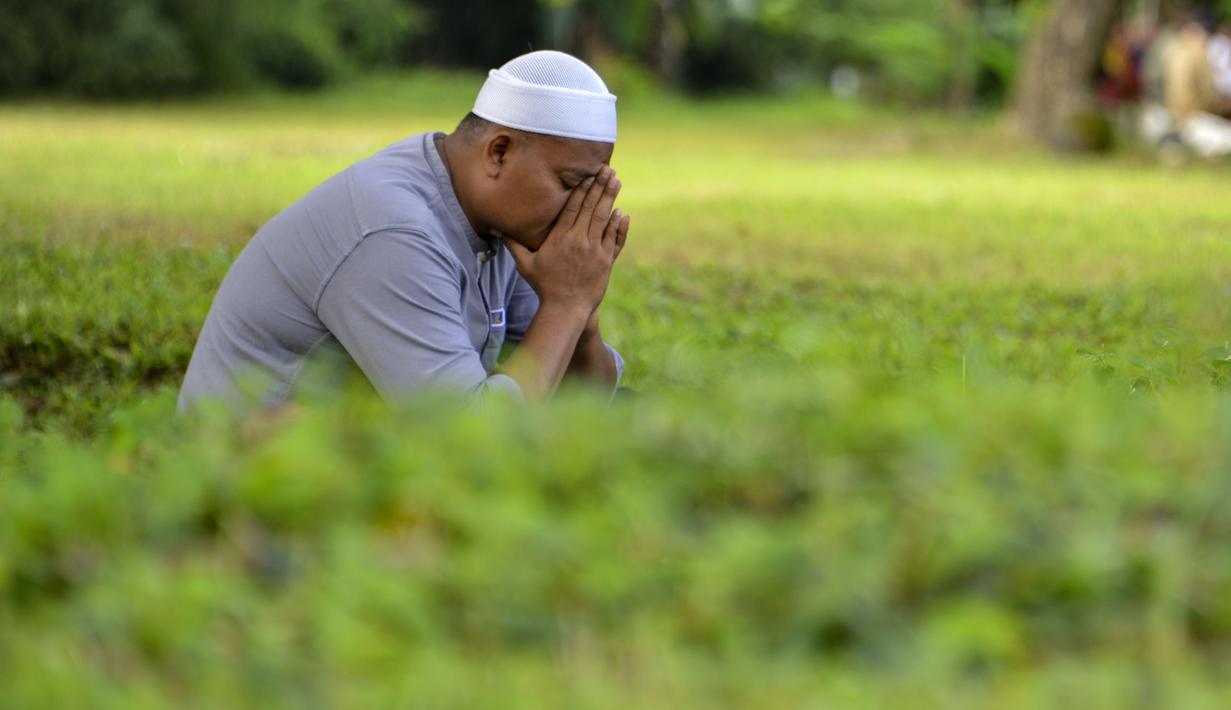 Seorang pria berdoa saat melakukan ziarah pada peringatan 16 tahun gempa bumi dan tsunami Aceh di sebuah kuburan massal di Siron, Sabtu (26/12/2020).  Peringatan di tengah pandemi COVID-19 itu tetap berlangsung secara sederhana melalui kegiatan ziarah kubur. (CHAIDEER MAHYUDDIN/AFP)