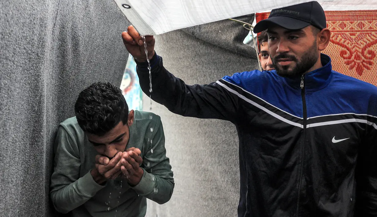 Salah satu pengungsi menggunakan tangan untuk meminum air hujan yang menetes dari atap tenda pengungsian yang dikelola oleh Badan Bantuan dan Pekerjaan Perserikatan Bangsa-Bangsa (PBB) untuk Pengungsi Palestina di Rafah, Jalur Gaza Selatan pada 14 November 2023. (SAID KHATIB/AFP)