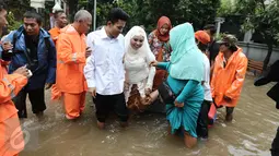 Keluarga pengantin dan pengantin Mansur dan Maya di evakuasi pasukan orange seusai melakukan akad nikah di KUA Mampang Prapatan, Jakarta, Selasa (21/2). Walaupun banjir sepasang pengantin ini tetap melakukan akad nikah. (Liputan6.com/Herman Zakharia)