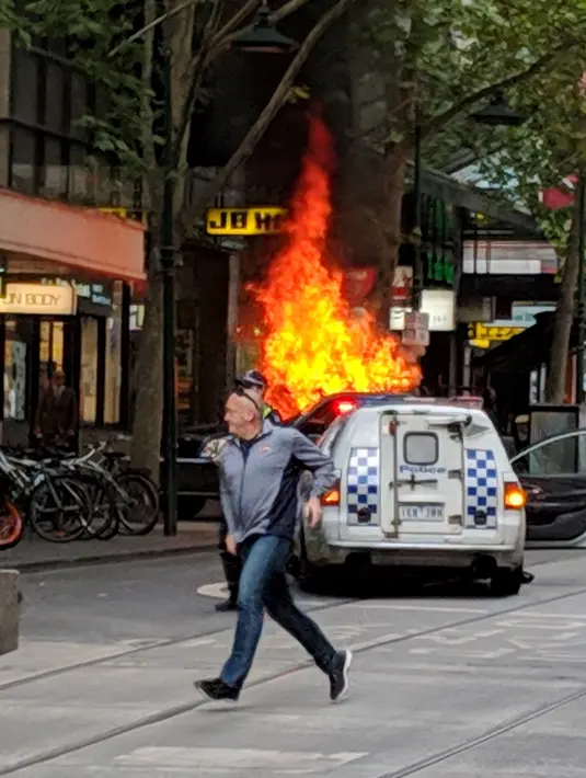 Seorang pria berlari dekat kendaraan yang terbakar setelah pengemudi menghentikan kendaraan dan menikam sejumlah orang di pusat Kota Melbourne, Australia, Jumat (9/11). (Chris Newport/Courtesy of Chris Newport via Instagram/AFP)