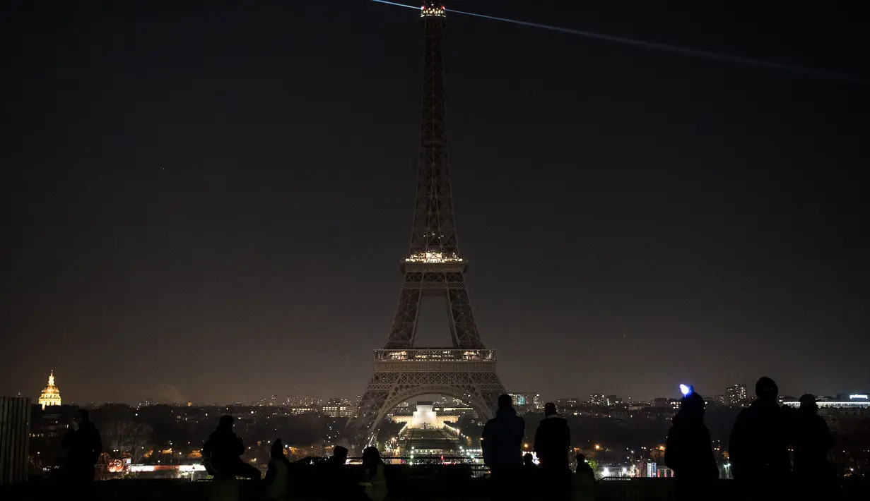 Sejumlah wisatawan mengamati pemadaman lampu di Menara Eiffel, Paris, Rabu (14/12). Lampu menara ikonik setinggi 300 meter itu dimatikan pada Rabu malam untuk menunjukkan dukungan bagi warga Aleppo di Suriah. (AFP PHOTO/PHILIPPE LOPEZ)