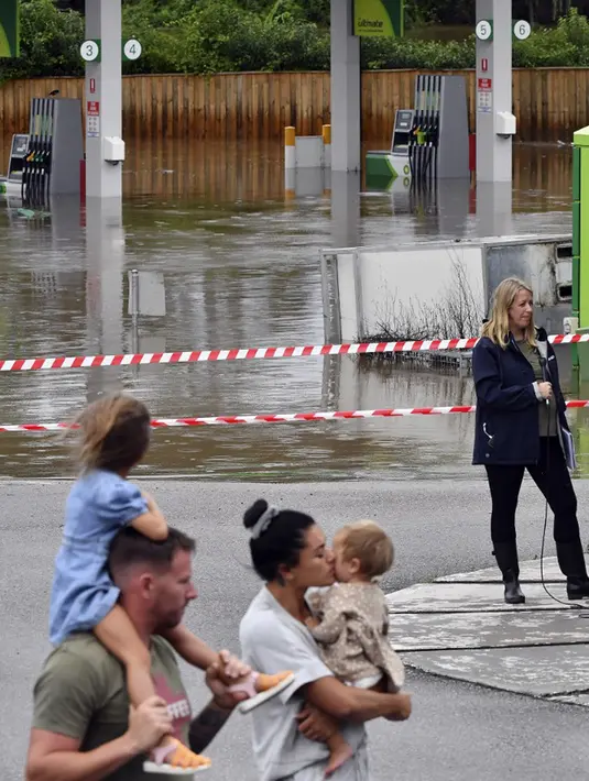 Sebuah keluarga berjalan melewati pompa bensin yang tidak tergenang oleh banjir di pinggiran barat daya Camden, Sydney, Australia, Selasa (8/3/2022). (Muhammad FAROOQ/AFP)