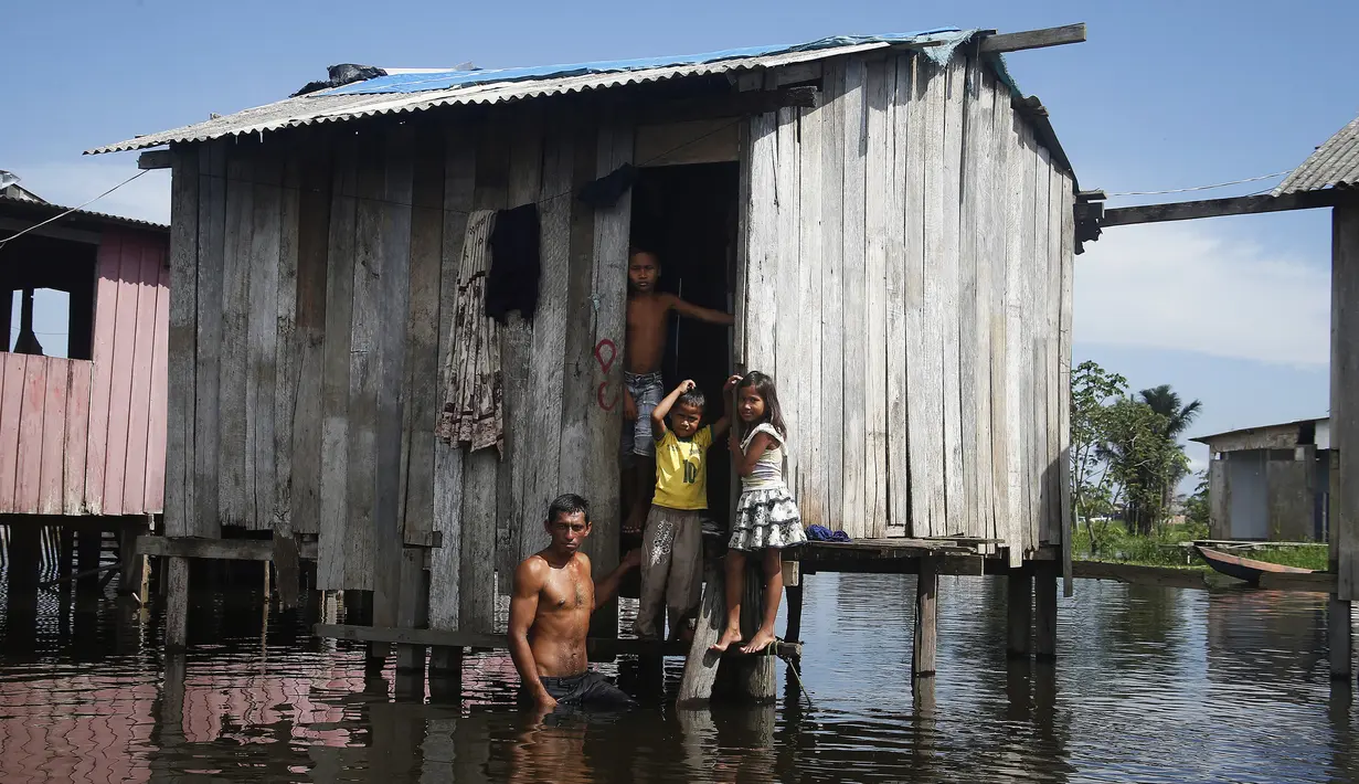 Francisco Fabiano Rodrigues dan anak-anaknya berdiri di teras rumah mereka di jalan yang dibanjiri oleh naiknya sungai Negro di Iranduba, negara bagian Amazonas, Brasil, Senin (23/5/2022). Wilayah Amazon sedang dilanda banjir dengan 35 kotamadya yang menghadapi salah satu banjir terburuk mereka dalam beberapa tahun dan permukaan air diperkirakan akan meningkat selama beberapa bulan mendatang. (AP Photo/Edmar Barros)