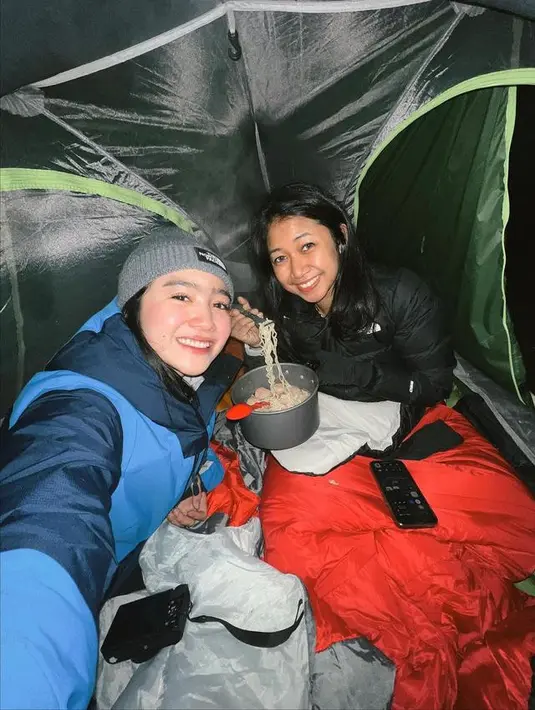 Febby Rastanty tersenyum saat menikmati mie instan bersama temannya yang bernama Bella di dalam tenda selama mendaki Gunung Merbabu dan mengunggah ke akun Instagram miliknya. (Instagram/febyraastanty)
