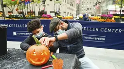 Sharif Butler dan keponakannya Chace mengukir labu di Rockefeller Center (22/10/2020). Para pekerja di Rockefeller Center beristirahat sejenak untuk mempelajari cara mengukir labu dengan benar dari Maniac Pumpkin Carvers, seniman dari Brooklyn . (Diane Bondareff/AP Images for Tishman Speyer)