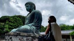 Seorang perempuan bermasker mengunjungi The Great Buddha atau yang biasa disebut Kamakura Daibutsu di kuil Kotoku-in di Kamakura, Prefektur Kanagawa, Jepang, Sabtu (20/6/2020). Patung Buddha dari perunggu yang menjulang dengan tinggi 13,35 meter ini didirikan tahun 1252. (Behrouz MEHRI/AFP)