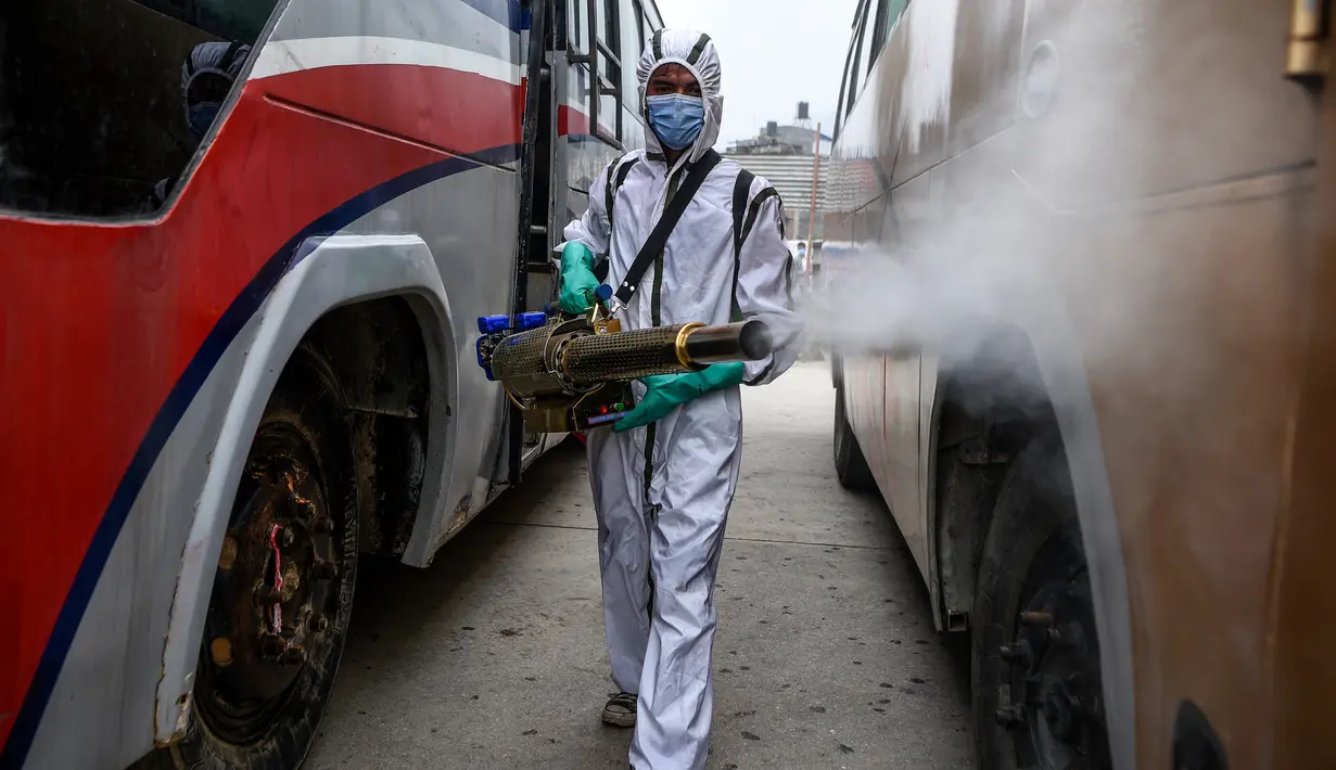 Pekerja yang mengenakan Alat Pelindung Diri (APD) menyemprotkan disinfektan pada bagian luar bus di Kathmandu, Kamis (17/9/2020). Pemerintah Nepal melonggarkan pembatasan yang diberlakukan sebagai tindakan pencegahan terhadap virus corona pada transportasi umum jarak jauh. (PRAKASH MATHEMA/AFP)