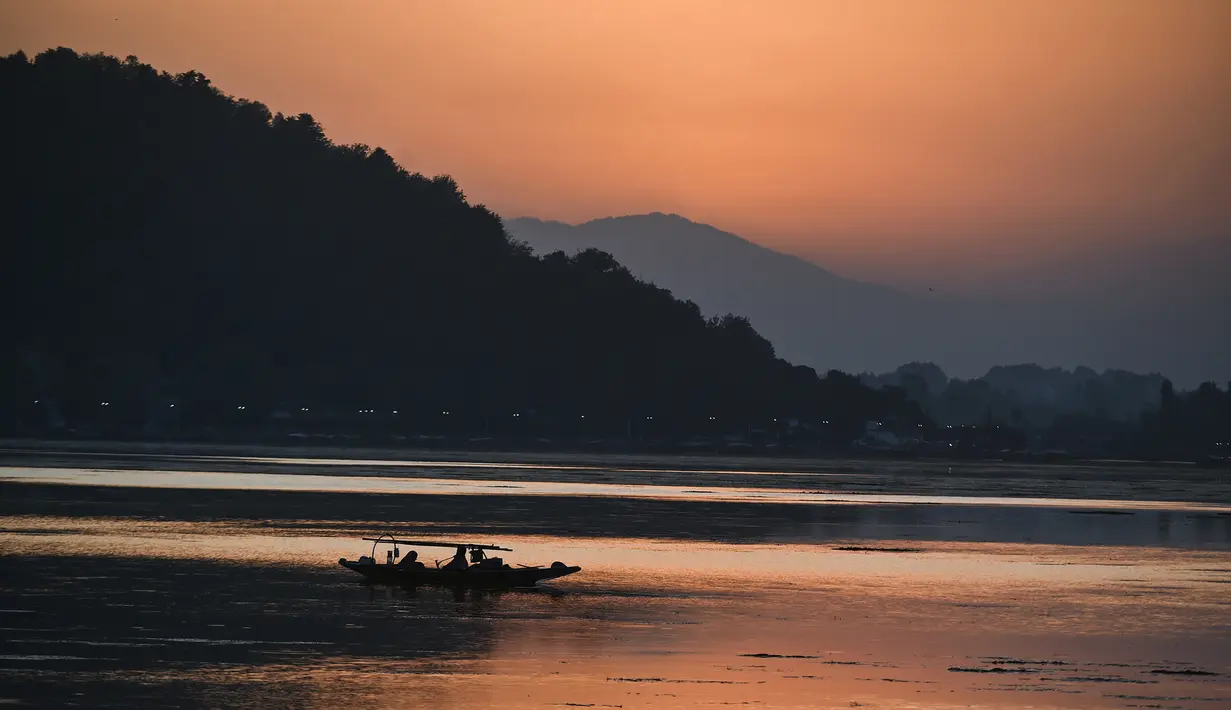 Nelayan menunggu di perahu kecil setelah memancing di Danau Dal saat matahari terbenam di Srinagar (9/9/2019). Danau Dal yang luas dan bening. Diatasnya terhampar gerombolan daun bunga lotus. (AFP Photo/Tauseef Mustafa)