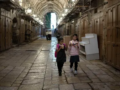 Gadis-gadis Palestina makan mie saat mereka berjalan pulang dari sekolah melalui deretan toko yang ditutup untuk pemogokan umum yang menyerukan gencatan senjata di Gaza di Kota Tua Yerusalem, Senin (11/12/2023). (AP Photo/Maya Alleruzzo)