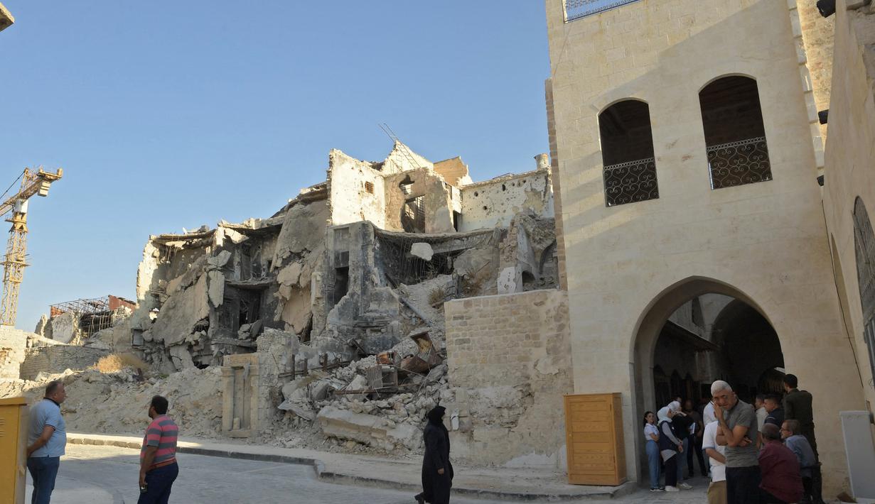 Orang-orang berjalan melewati bangunan yang runtuh di "Souq Khan al-Harir" (pasar tertutup sutra) yang dibuka kembali setelah upaya rekonstruksi setelah konflik bertahun-tahun di kota utara Aleppo, Suriah (29/8/2021). (AFP Photo)
