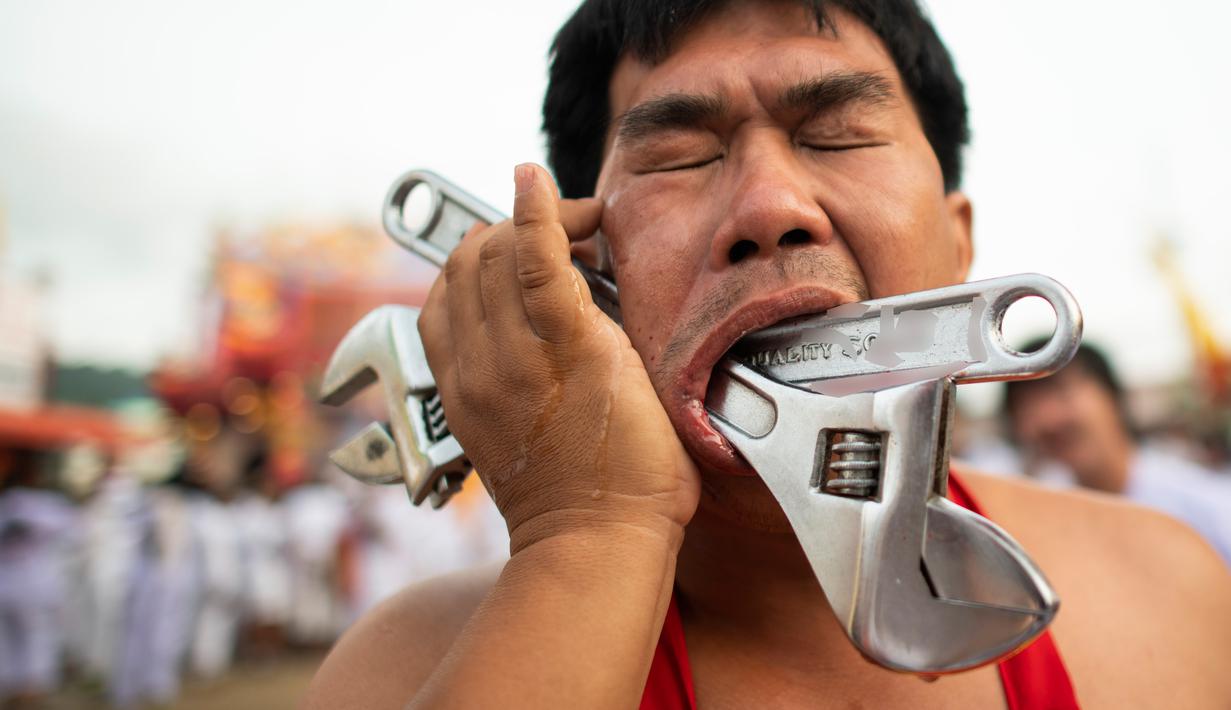 Penganut kuil Loem Hu Thai Su menusukkan kunci inggris ke pipinya saat festival vegetarian tahunan di Phuket, Thailand, Jumat (12/10). Acara ini dikenal juga dengan 'Nine Emperor Gods' atau hari 'Sembilan Kaisar Dewa'. (Jewel Samad/AFP)