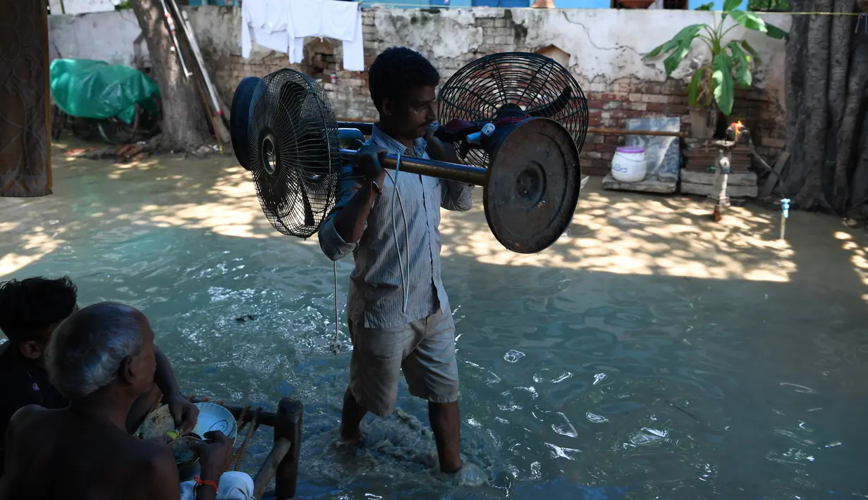 Seorang lelaki membawa kipas angin listrik saat melintasi banjir di daerah perumahan dekat tepi Sungai Yamuna yang meluap di New Delhi, India, Selasa (20/8/2019). (AFP Photo/Sajjad Hussain)