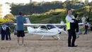 Orang-orang berdiri di dekat sebuah pesawat ringan yang mendarat darurat di sebuah pantai di Sydney, Rabu (26/5/2021). Pesawat kategori rekreasi itu mendarat selamat di pantai Sydney dengan tiga orang di dalamnya termasuk seorang bayi setelah mengalami kerusakan mesin. (AP Photo/Mark Baker)