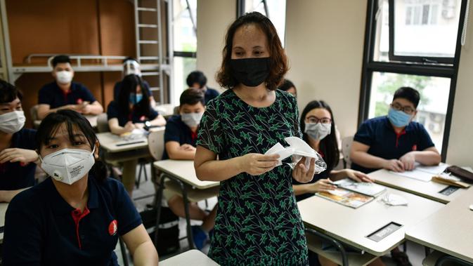 Seorang guru membagikan masker kepada siswa di dalam kelas di sekolah Marie Curie di Hanoi, Senin (4/5/2020). Vietnam membuka kembali aktivitas sekolah yang ditutup selama tiga bulan setelah dilaporkan tidak ada kasus virus corona COVID-19 baru hingga Sabtu, 2 Mei 2020. (Manan VATSYAYANA/AFP)