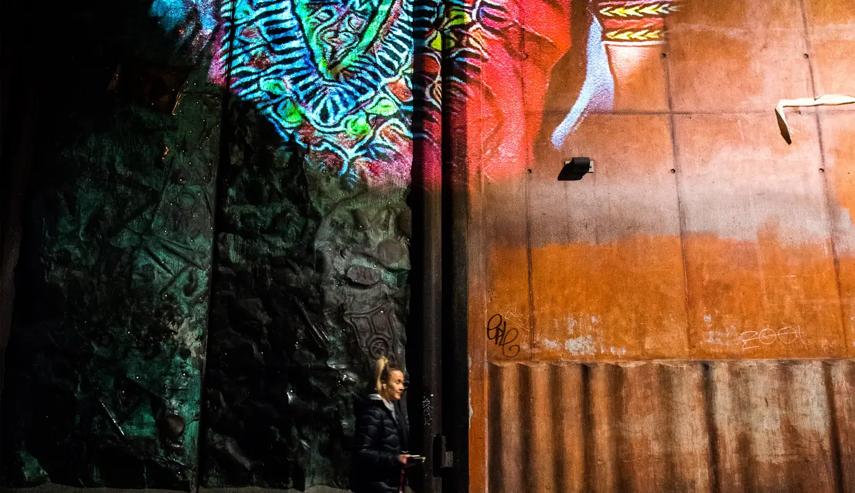 Seorang wanita berjalan dibawah karya seniman Prancis, Julien Nonnon yang menghiasi tembok sebuah bangunan di Sodermalm, Stockholm, Swedia (25/11). (AFP/Jonathan Nackstrand)