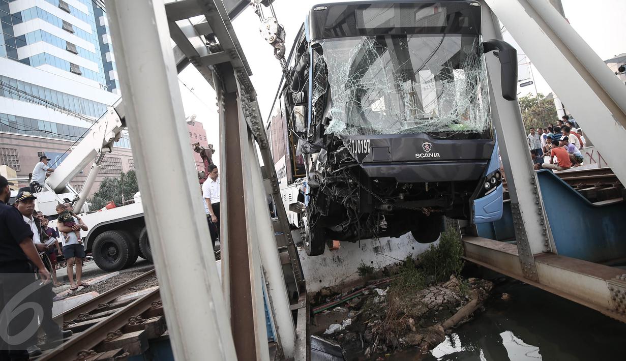 Alat berat mengangkat badan bus transjakarta yang terperosok ke sungai usai ditabrak kereta Senja Utama Solo di perlintasan Jalan Mangga Dua, Jakarta, Kamis (19/5). Sopir Transjakarta, Adil Setiawan mengalami luka berat. (Liputan6.com/Faizal Fanani)