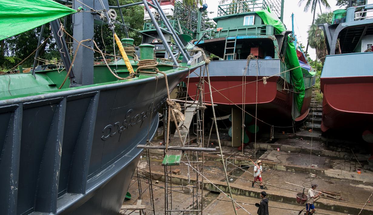 Para pekerja berjalan melewati kapal-kapal yang sedang diperbaiki di galangan kapal di tepi Sungai Yangon, yang terletak di pinggiran Yangon, Myanmar (30/7/2019). (AFP Phot/Sai Aung Main)