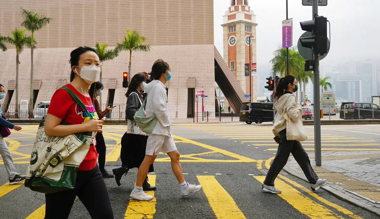 Orang-orang yang memakai masker berjalan di sepanjang jalan di Hong Kong, Jumat (28/1/2022). Hong Kong memangkas masa karantina wajib bagi orang-orang yang datang dari luar negeri dari 21 menjadi 14 hari. (AP Photo/Kin Cheung)