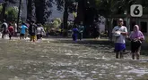 Warga melintasi genangan air yang merendam jalan di kawasan Kampung Makasar, Jakarta Timur, Senin (7/7/2025). (Liputan6.com/Herman Zakharia)