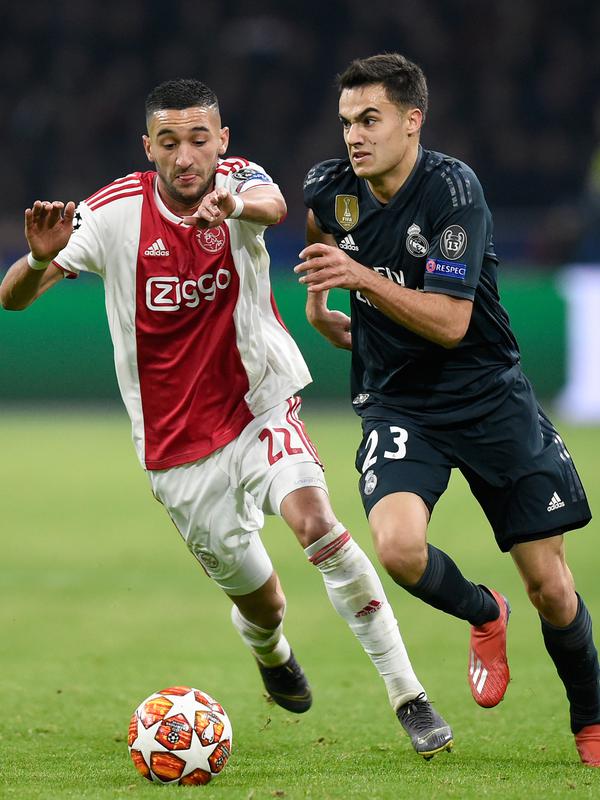 Gelandang Ajax, Hakim Ziyech berebut bola dengan bek Real Madrid, Sergio Reguilon pada leg pertama 16 besar Liga Champions di Johan Cruijff ArenA, Rabu (13/2). Real Madrid harus bersusah payah menaklukkan Ajax dengan skor tipis 2-1. (JOHN THYS / AFP)