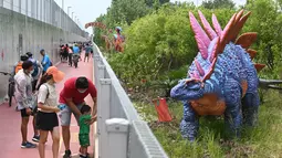 Orang-orang berhenti untuk mengambil foto replika dinosaurus seukuran aslinya yang dipajang di sepanjang "Changi Jurassic Mile" jalan santai di Singapura (13/10/2020). Ada 22 replika dinosaurus yang dibangun di jalur Bandara Changi dengan East Coast Park. (AFP/Roslan Rahman)