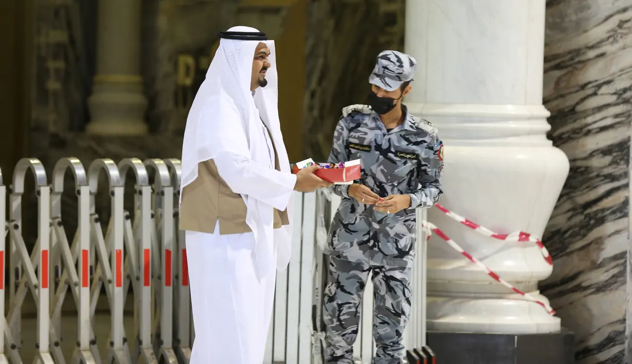 Seorang jemaah menawarkan manisan kepada penjaga keamanan saat pelaksanaan salat Idul Fitri di Masjidil Haram, Mekah, Arab Saudi, Minggu (24/5/2020). Salat Idul Fitri tetap digelar di Masjidil Haram dan Masjid Nabawi namun dengan jemaah terbatas. (STR/AFP)